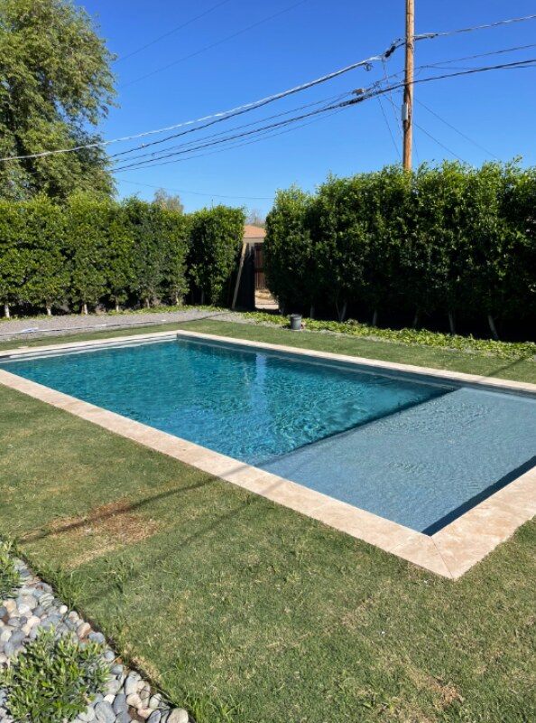 Filled rectangular pool with travertine coping bordered by lawn and a tall hedge