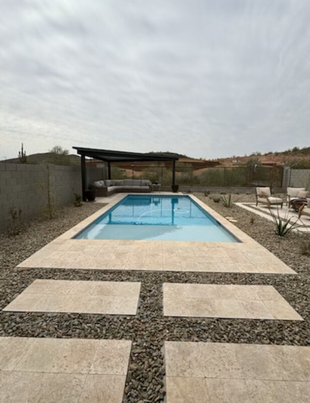 Rectangular pool with travertine decking, a ramada and desert landscaping in an Arizona backyard