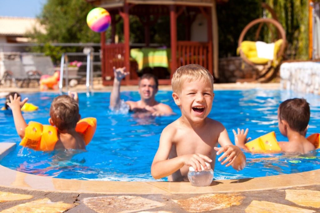 Children and an adult playing with a beach ball in a backyard swimming pool