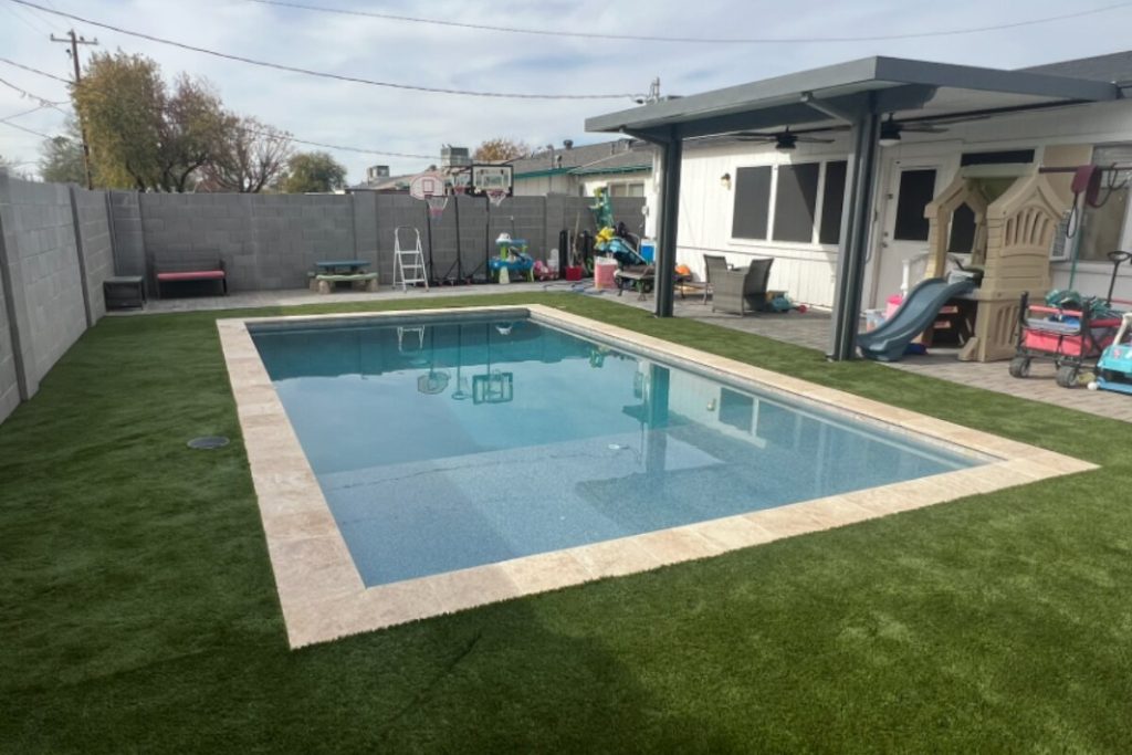 Finished rectangular pool with travertine coping and artificial turf in a Phoenix backyard